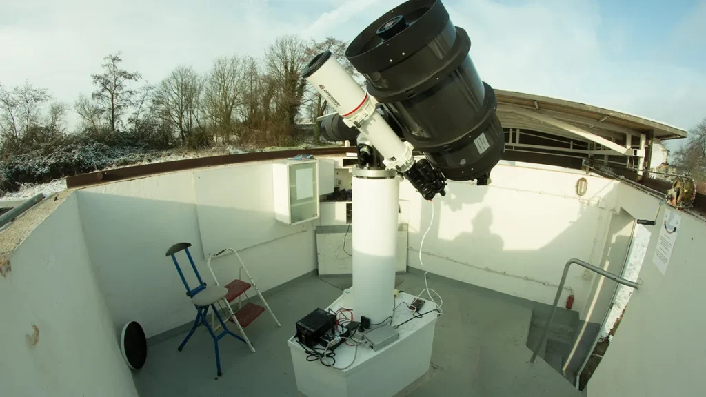 Large black telescope on a white pier next to a smaller white refractor inside a concrete observatory pit.