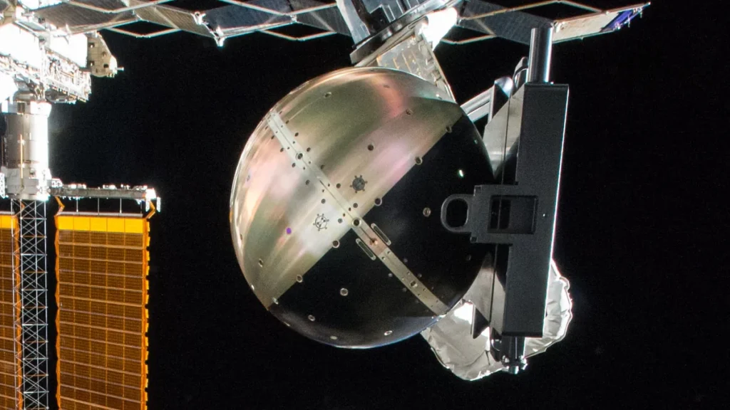 Spherical metallic space hardware attached to the ISS structure with golden solar panels in the background.