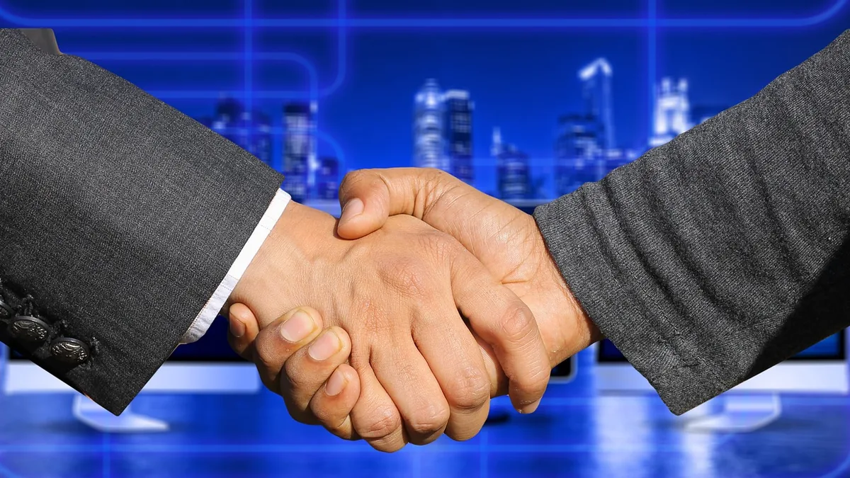 Handshake in suits against a blue digital background, representing collaboration and merger.