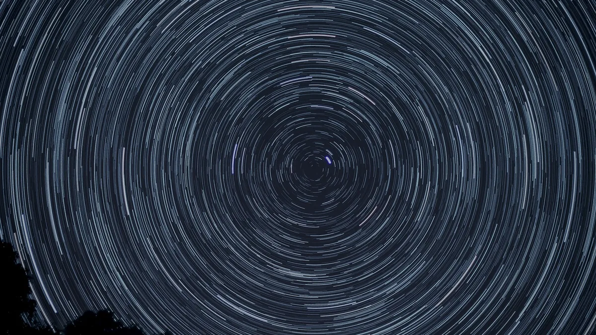 Concentric star trails form circular patterns across a dark blue night sky.