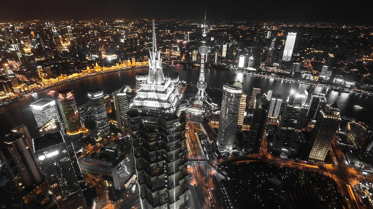 A high-angle night view of Shanghai's brightly lit skyline, featuring towering skyscrapers and the Oriental Pearl Tower.