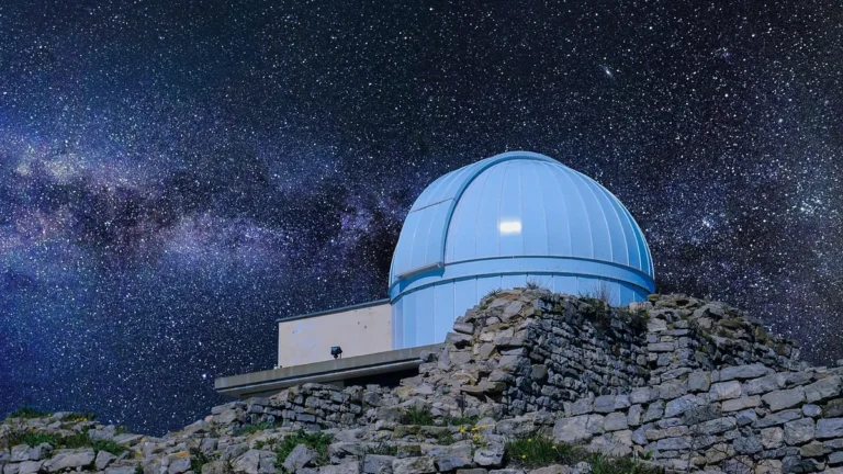 A blue observatory dome on a stone wall under a starry sky with the Milky Way.