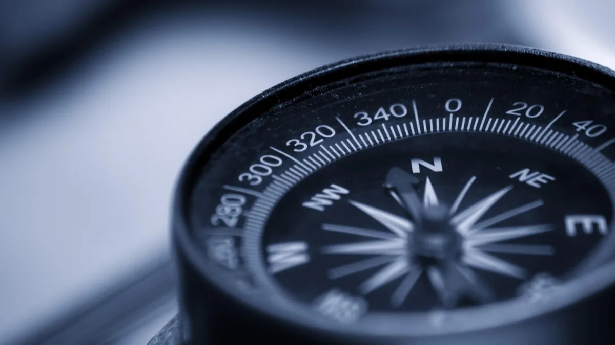 Close-up of a black compass dial showing degrees and cardinal directions in cool blue light.