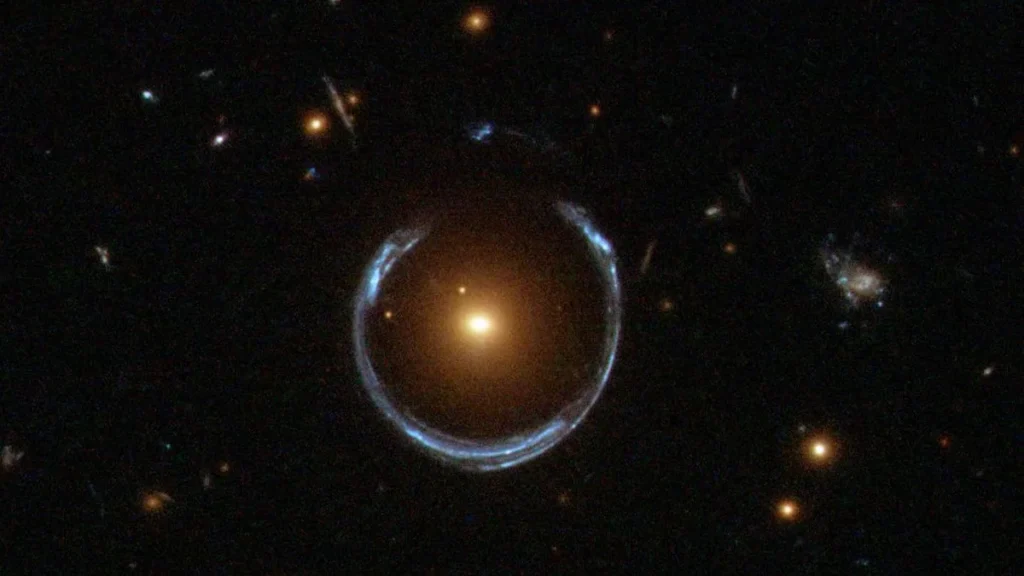 A vibrant blue Einstein ring encircles a bright orange galaxy, showcasing the power of cosmic gravitational lensing.
