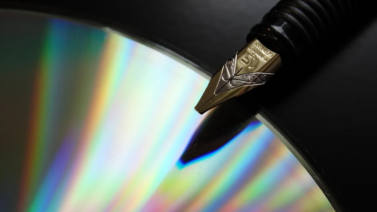 Macro close-up of a gold fountain pen nib resting on a reflective CD showing vibrant rainbow spectral colors.