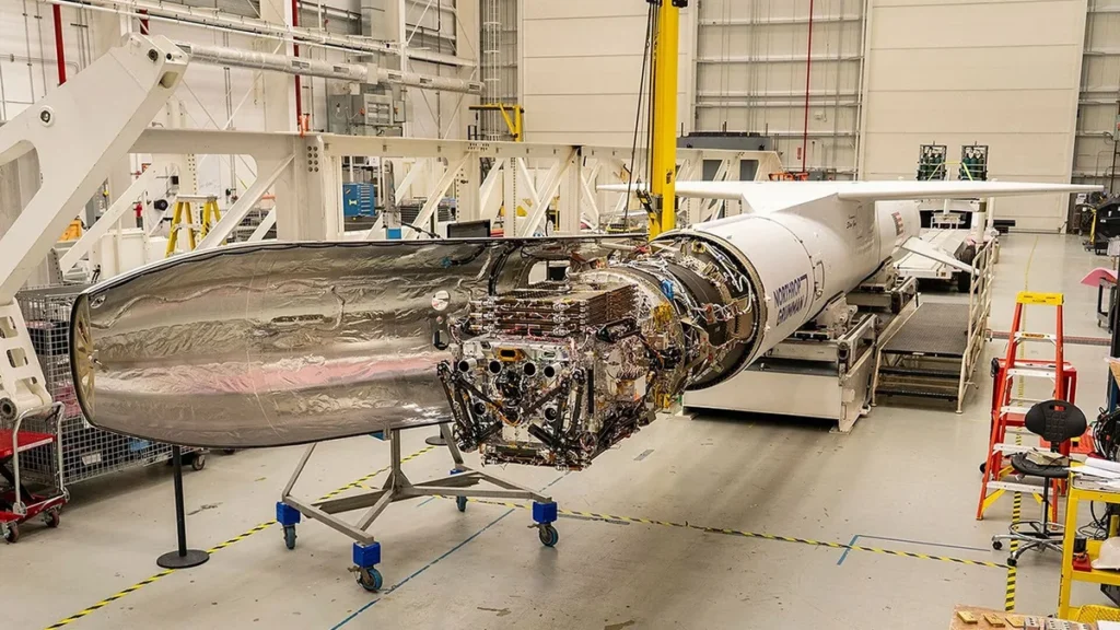Complex space payload with exposed electronics and silver fairing inside a cleanroom facility.