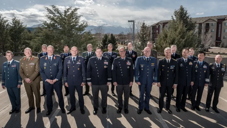 Military space leaders in formal uniforms pose for a group photo outdoors with mountains in the background.
