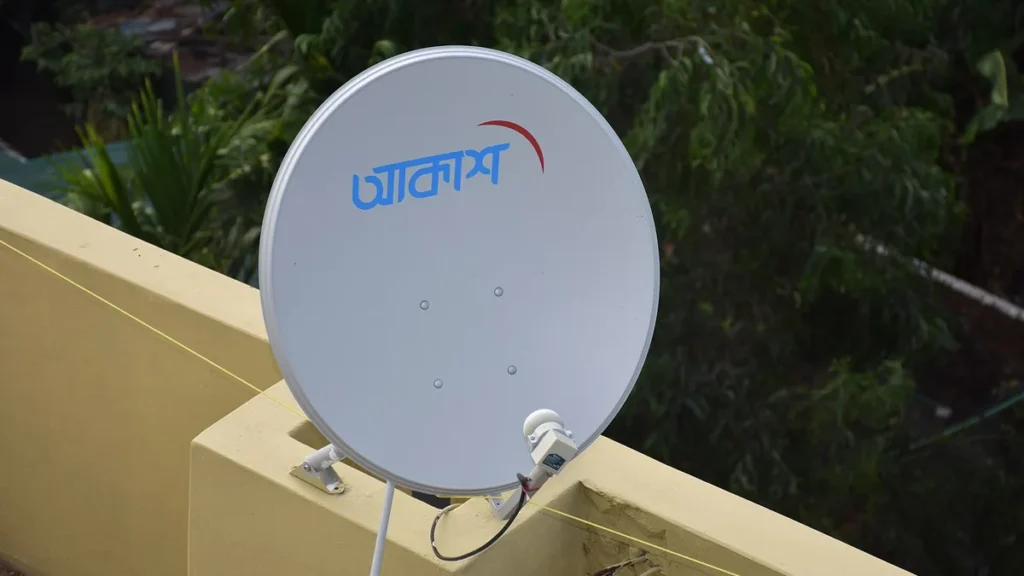 White satellite dish with blue Bengali logo and red crescent, mounted on a yellow rooftop wall.