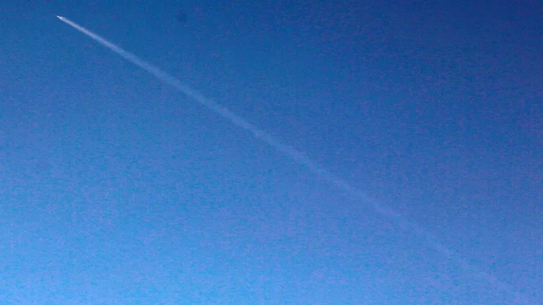 A bright rocket leaves a long white vapor trail streaking diagonally across a deep blue sky.