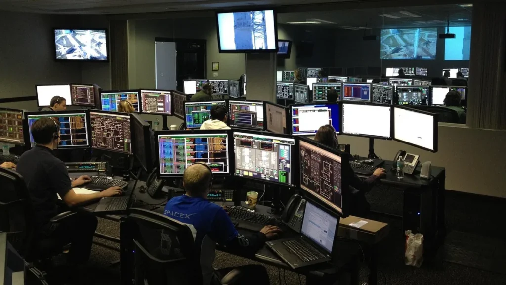 SpaceX staff monitor multiple screens displaying telemetry data in a control room filled with technical readouts.