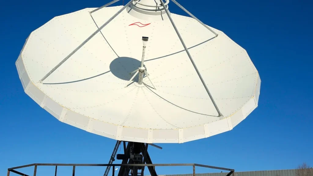 Large white parabolic satellite dish antenna set against a vibrant, clear blue sky, showing ground station infrastructure.