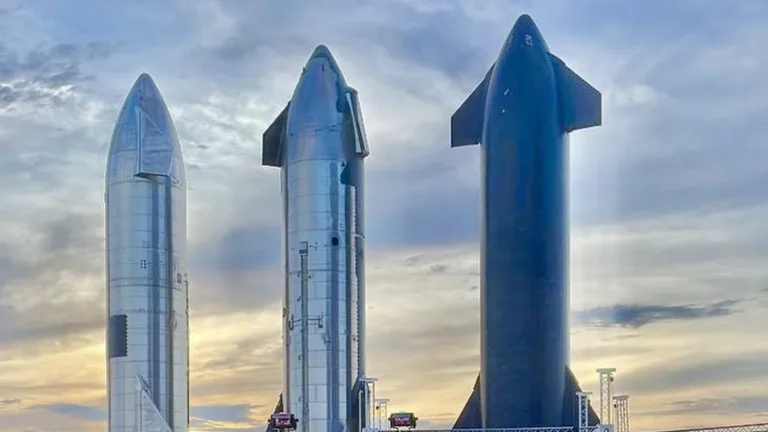 Three SpaceX Starship rockets stand against a cloudy sky, showing metallic and dark-colored hulls.