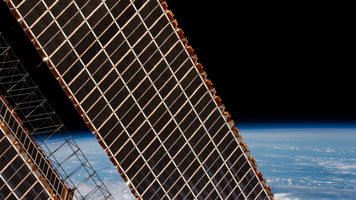 A close-up view of a large solar panel array in orbit with Earth and black space in the background.