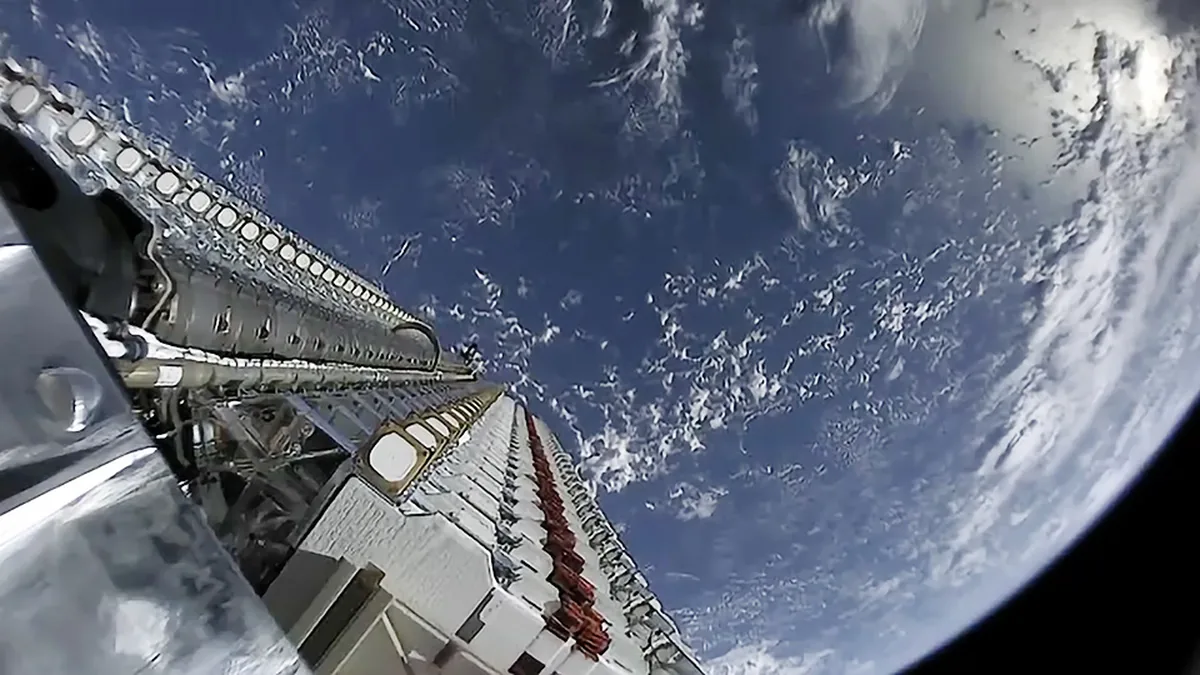 Wide-angle view of a Starlink satellite train deployed against the blue curve of Earth and clouds.