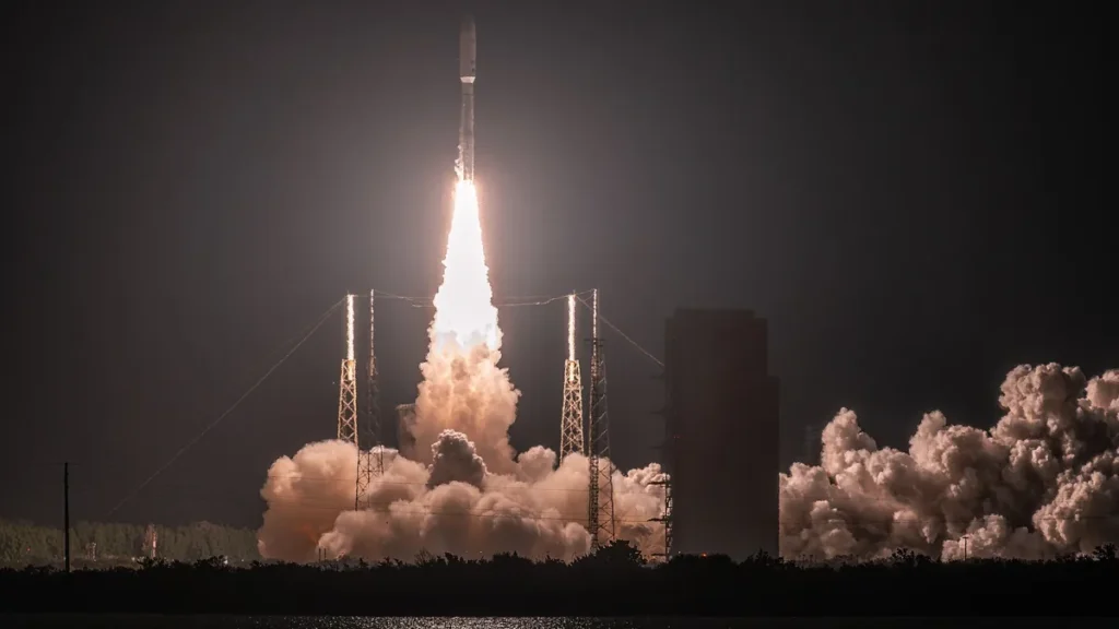 A rocket launches into the dark night, leaving a bright column of fire and huge clouds of billowing smoke.