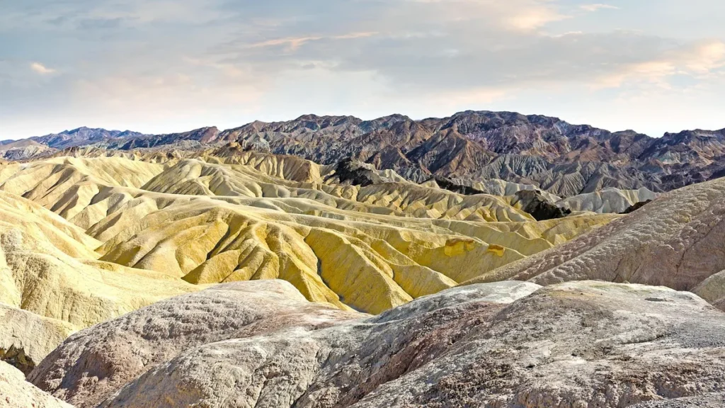 Vibrant yellow and beige eroded badlands stretch toward dark mountains under a soft cloudy sky.