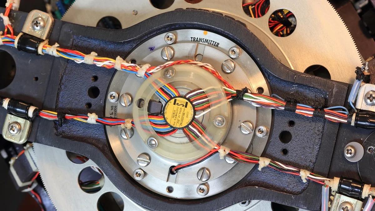 Close-up of a colorful wired transmitter assembly with a yellow label, part of a precision robotic mechanism.
