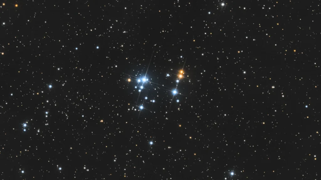 A dense cluster of bright blue and orange stars shines in the vastness of dark space.