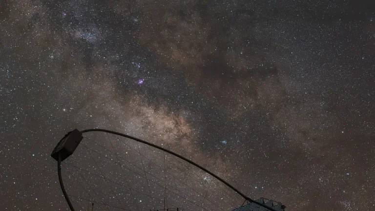 Silhouette of a telescope dish under the starry Milky Way galaxy.