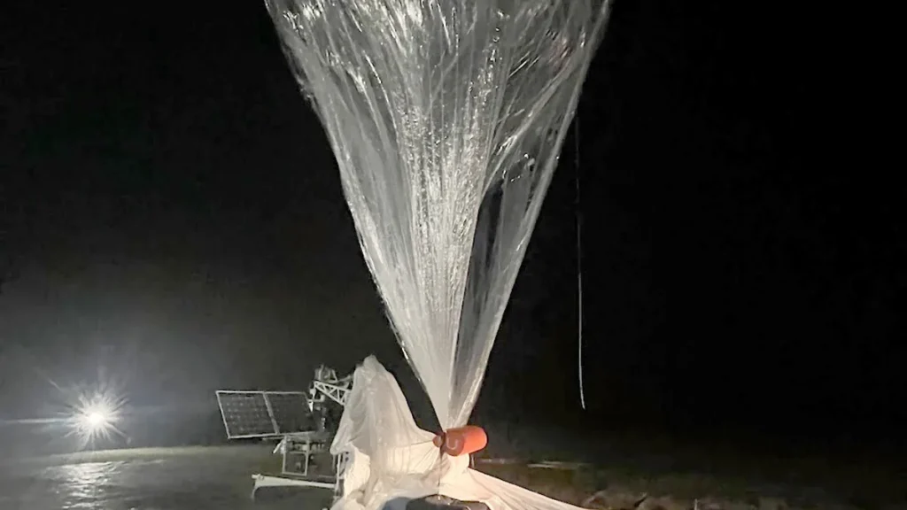 A large plastic scientific balloon inflating and rising into the dark night sky during a launch.