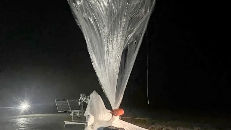 A large plastic scientific balloon inflating and rising into the dark night sky during a launch.
