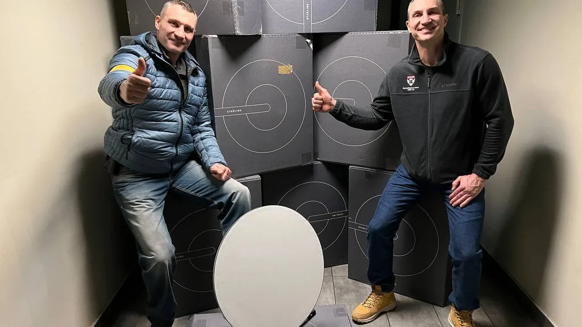 Kyiv Mayor Vitali Klitschko and an official pose with Starlink boxes and a dish, giving thumbs up.