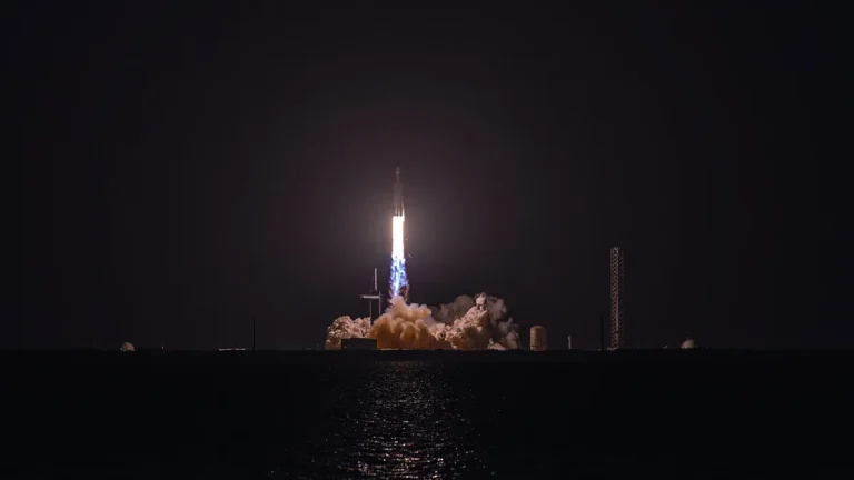 A rocket launches into the night sky, with bright fire and billowing smoke reflecting on the water below.