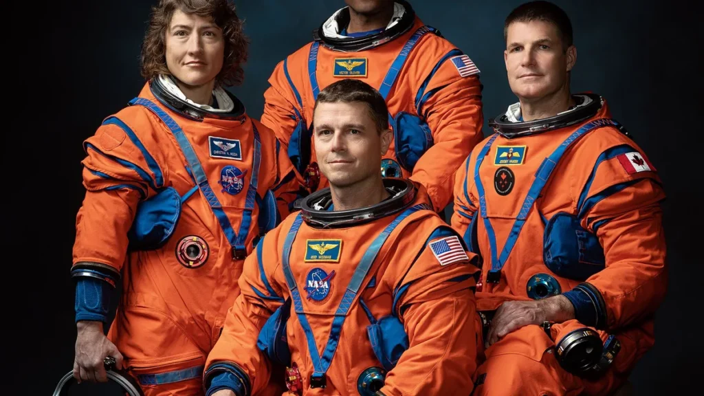 Artemis II crew members in orange spacesuits pose for an official portrait against a dark background.
