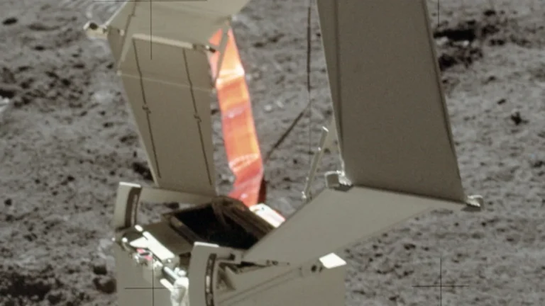Lunar surface hardware with deployed solar panels, orange ribbon, and camera crosshairs against grey dust.