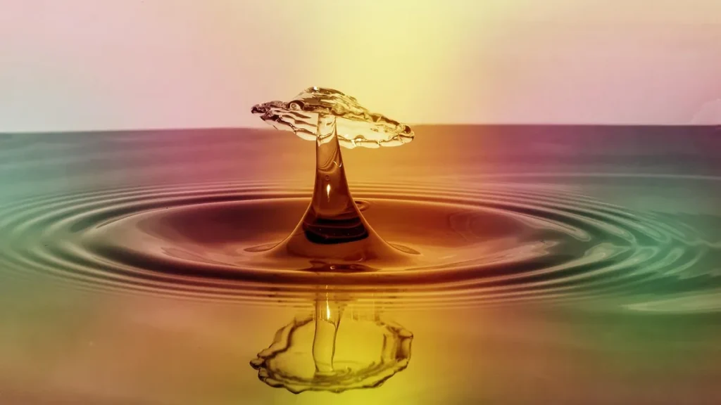 Macro shot of a colorful crown-shaped water droplet splash with ripples and reflection on a vibrant gradient background.