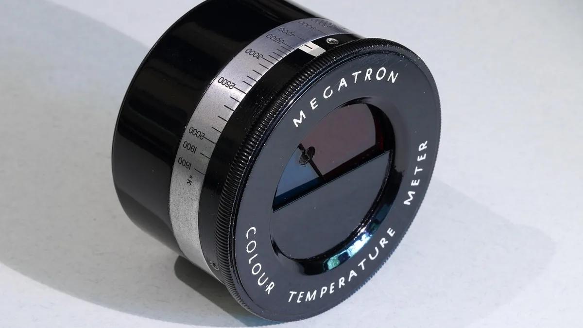 A vintage black Megatron colour temperature meter with a silver Kelvin scale on a white surface.