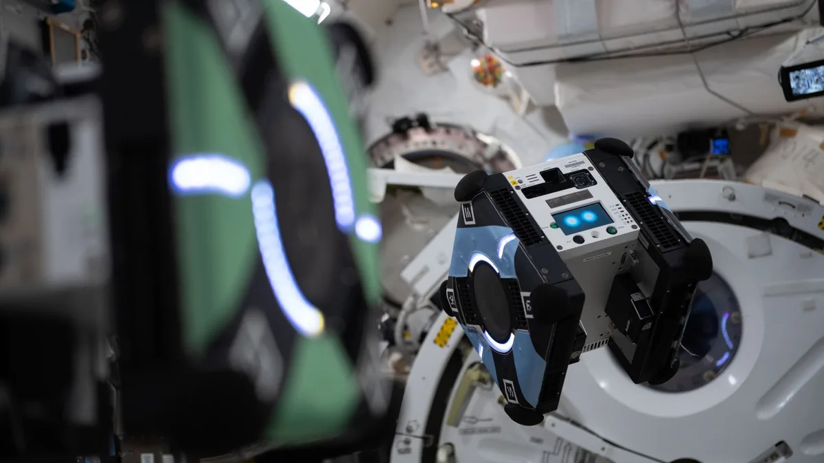 Two cube-shaped robotic satellites with glowing LED rings float inside a space station module.