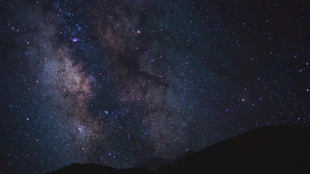 Starry night sky with the Milky Way galaxy glowing over a dark silhouette of hills.